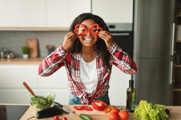 Happy young african american woman puts pepper pieces to her eyes like glasses and have fun in kitchen