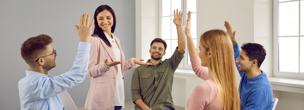 Banner narrow shot of diverse employees raise hands participate in teambuilding activity at meeting. Businesspeople communicate give feedback to female leader or coach. Briefing vote.
