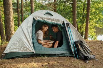 Portrait of couple of travelers dating in forest trip with tent and book in summertime.