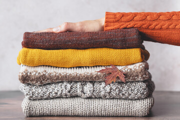 Bunch of knitted warm sweaters, females's hand on stack clothes of the autumn color palette. Faded retro style image. Sweater weather outfits. Fashion and sustainability life