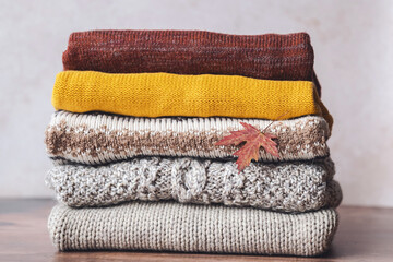 A stack of autumn warm clothes with a fallen leaf. Autumn color palette. used sweaters. Fashion and...