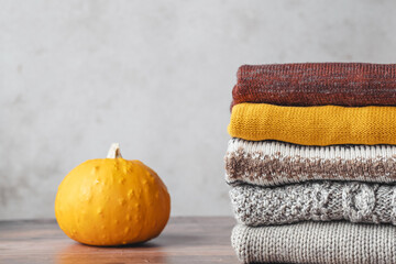 A stack of autumn warm clothes with pumpkin on a wooden table. Autumn color palette. Fashion and sustainability life
