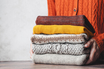 A woman holding a stack autumn warm knitted sweaters. Change of season and wardrobe. autumn slow...