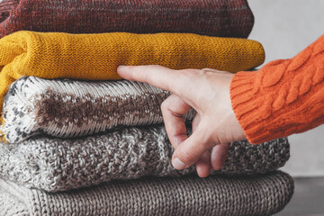 Female's hand pointing a finger at an autumn palette of warm knitted sweaters. used sweaters. autumn slow fashion concept