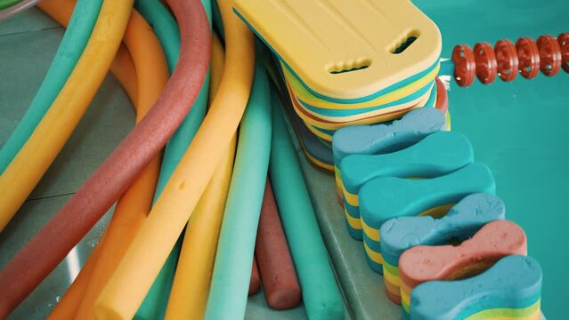 Items for swimming. Swimming boards, aqua noodles and buoys by the pool on tiles. Accessories for swimming. Tools for aerobics and swimming training. Swimming lessons. 