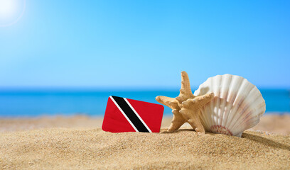 Fototapeta na wymiar Tropical beach with seashells and Trinidad and Tobago flag. The concept of a paradise vacation on the beaches of Trinidad and Tobago.