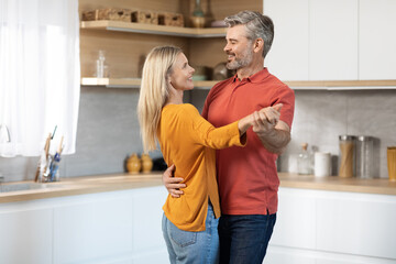 Beautiful mature spouses dancing together at kitchen