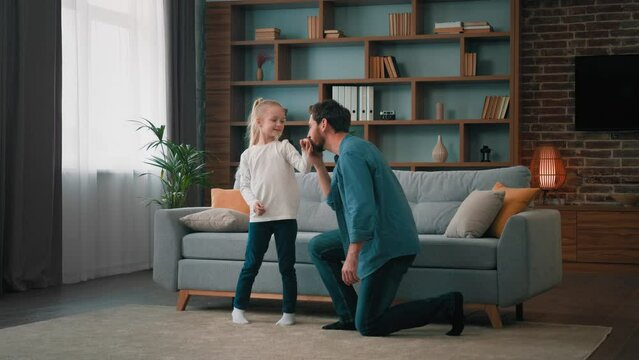 Loving young father dancing with cute child daughter family hobby weekend pastime at home daddy spin little girl in dance stand on one knee as prince kiss small hand thankful gesture parental caress