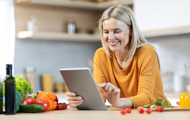 Cheerful blonde woman reading food blog and cooking
