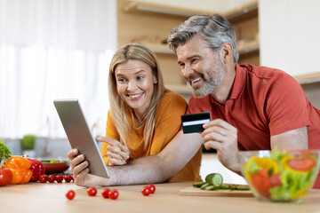Happy middle aged couple using digital tablet and credit card