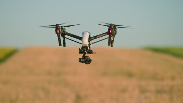 View of drone with digital video camera flying above field in harvest on blurred background. Blue sky. Outdoor. Shooting of quadcopter. Out of town. Village, Farmland. Terrain scanning technology