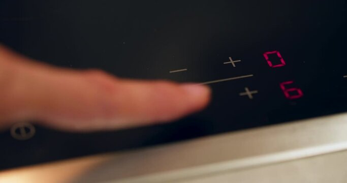 Woman turns on an electric induction cooker. Touch black electric panel. Switching on the burner cooktop Extreme close-up shot