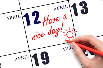 The hand writing the text Have a nice day and drawing the sun on the calendar date April 12