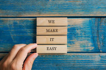 Male hand stacking four wooden pegs to make a We make it easy sign