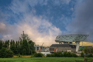 Foto op Aluminium Antwerpen, Vlaanderen, België - 10 juli 2022: in de buurt van Siberiabrug. Historische en moderne architectuur gecombineerd tot het creëren van een gebouw van het Havenbedrijf onder zonsopgang blauwe hemel. Groen blad vooraan © Klodien