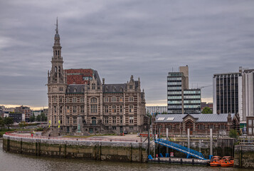 Antwerpen, Flanders, Belgium - July 10, 2022: Along Scheldt River. Beige-brown stone Historic Loodswezen, shipping pilots, facade under gray cloudscape. Memorial for lost sailors and more