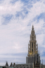 Fototapeta premium Antwerpen, Flanders, Belgium - July 10, 2022: Seen from Scheldt River. Closeup of Notre Dame Cathedral clock tower under blue cloudscape. Scaffold at bottom