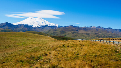 Wavy road through the autumn hills to the distant snowy mountain