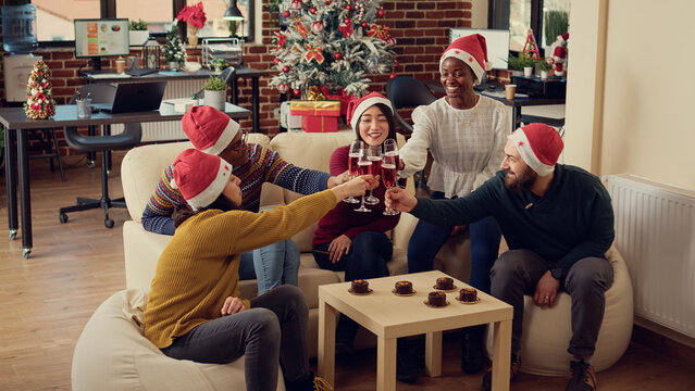 Multiethnic Group Of People Clinking Glasses Of Wine During Office Christmas Party, Giving Toast To Celebrate Winter Holiday. Celebrating Seasonal Festivity With Alcoholic Drinks, Saying Cheers.
