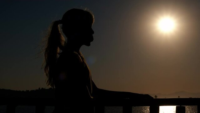 Child silhouette with bubble by sea. A young girl silhouette making a bubble gum against sunset by the sea. A concept of relaxation during summer vacation.