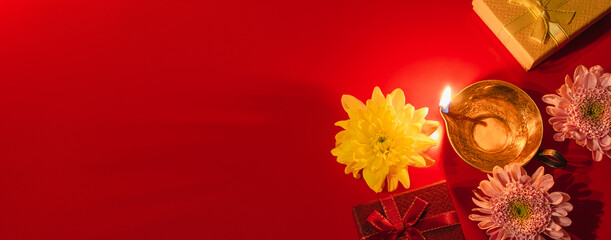 Happy Diwali. Diya oil lamp, flowers and gift boxes on red background. Celebrating the Indian traditional festival of light. Copy space.