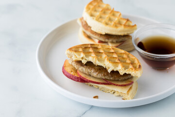A toasted waffle and sausage sandwich served with maple syrup for dipping.