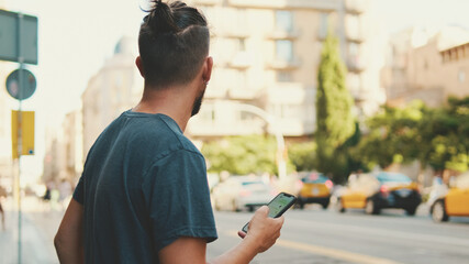 Young man with beard is using cellphone on the background of passing cars