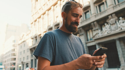 Young man with beard walks down the street using cellphone