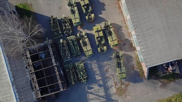 Aerial view of military equipment that stands on a concrete platform. The camera smoothly moves away from the ground when shooting