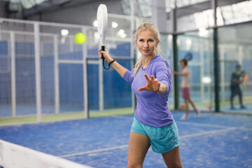 European woman serving ball while playing padel in court during training.