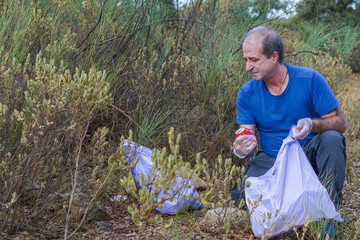 man crouching with garbage bags cleaning up the waste mountain