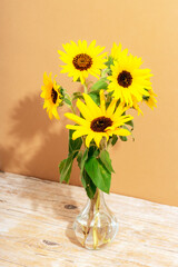 Bouquet of sunflowers in glass vase on wooden table. Closeup