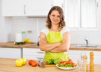 Young satisfied woman in apron preparing vegetable salad