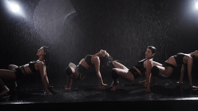 Four sexy young women standing in a row and dancing under the rain