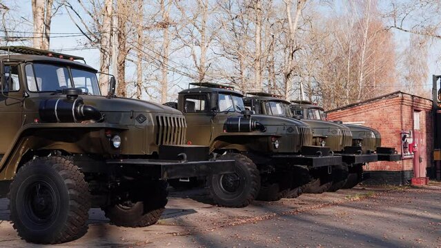 Several military trucks are standing on the asphalt platform and are arranged in a row. Smooth camera movement