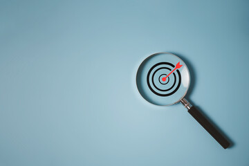 Target board inside of magnifier glass for focus business objective achievement concept on blue...