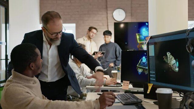 The CEO of the company studio developers of games and applications discusses with the artist a 3D model on a computer against the background of other employees of the company.