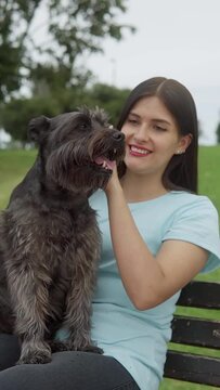 A Latin young adult woman pets her black schnauzer.