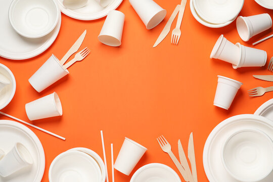 Frame of disposable tableware on orange background, flat lay. Space for text