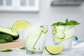 Tasty fresh cucumber water with sliced lime and basil on white table indoors
