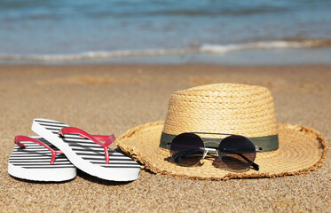 Striped flip flops, straw hat and sunglasses on sandy beach near sea