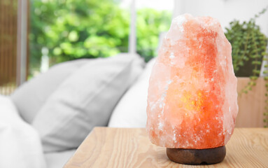 Himalayan salt lamp on wooden table in bedroom. Space for text