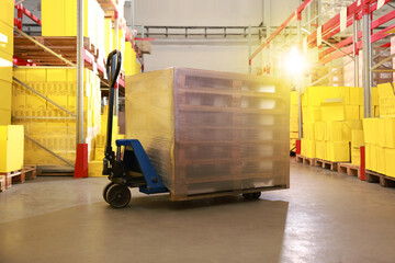 Naklejka premium Modern manual forklift with wrapped wooden pallets in warehouse
