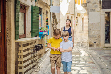 Mom and son travelers enjoying Colorful street in Old town of Kotor on a sunny day, Montenegro. Travel to Montenegro concept Portrait of a disgruntled girl sitting at a cafe table