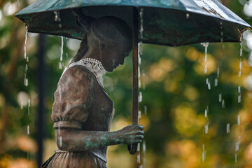 Rain falls on statue of a woman with umbrella and lace collar