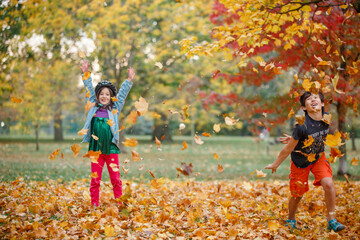 Two happy children play together in a pile of fall leaves