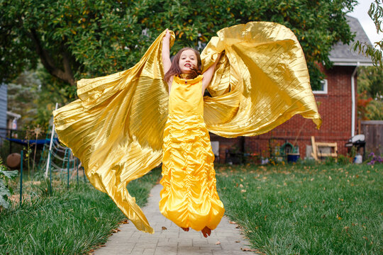 An angelic little girl in golden dress and long cape leaps in air