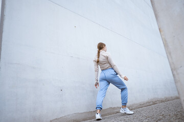 Girl in a blue pants stretching and dancing against grey wall