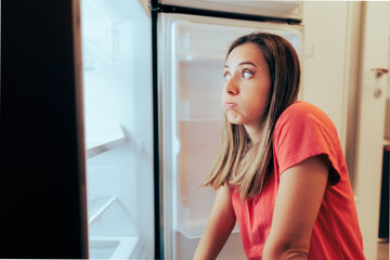 Hungry Woman Having Nothing to Eat Looking at Empty Fridge. Stressed girl feeling hungry looking inside the refrigerator
