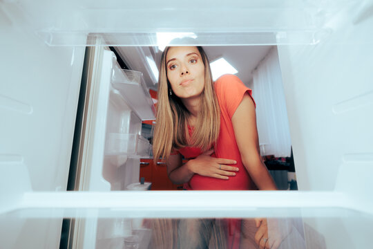 Pregnant Woman Craving For Food Looking At An Empty Fridge. Mother To Be Having Nothing To Eat Considering Ordering A Meal In
